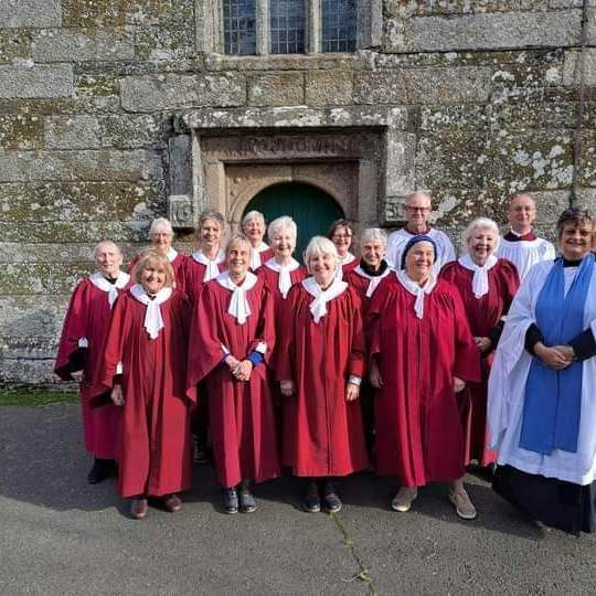 A church choir in red and white robes standing together in front of a stone church