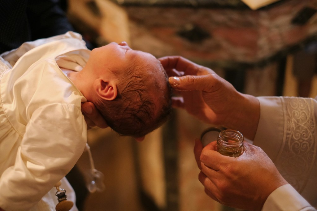 A baby in a white christening gown being anointed with oil at baptism